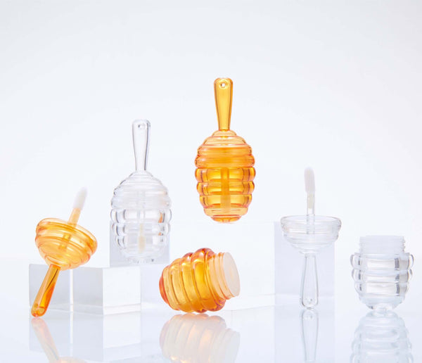 Mini Bee Fang honeycomb lip gloss tubes in clear and amber colors, featuring ergonomic applicators and stylish design.